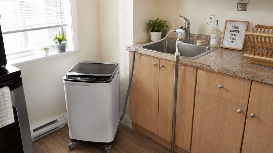 Portable washing machine connected to a kitchen sink faucet with a quick-connect hose in a small apartment