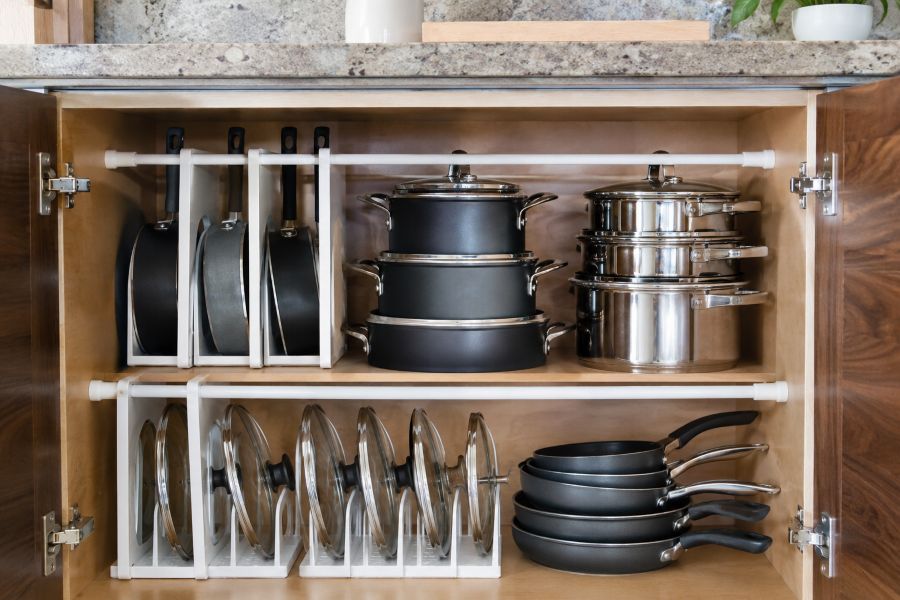 Organized kitchen cabinet interior with tension rods and stackable cookware