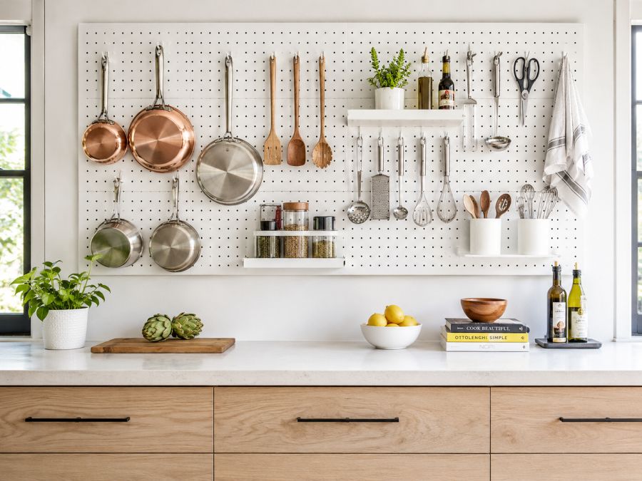 Kitchen pegboard system with customizable hooks displaying pots, pans, utensils, and kitchen tools above counter workspace